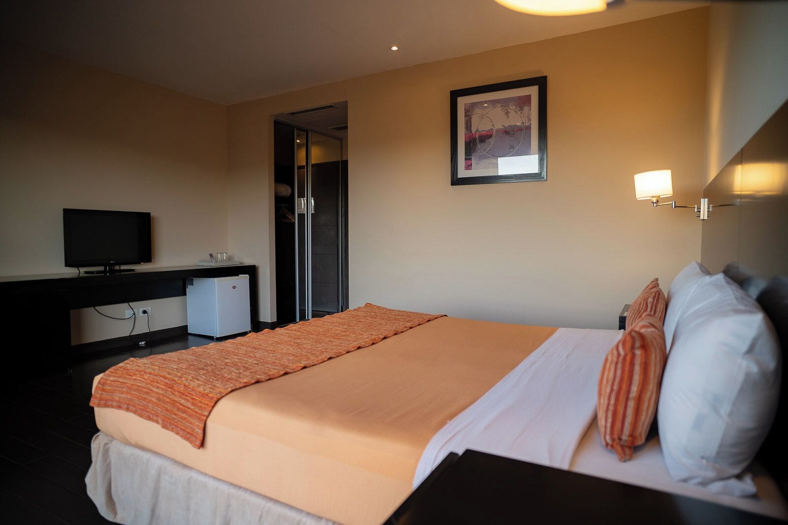 Habitación de hotel con cama, escritorio con televisor, refrigerador pequeño y puerta que da a un baño.