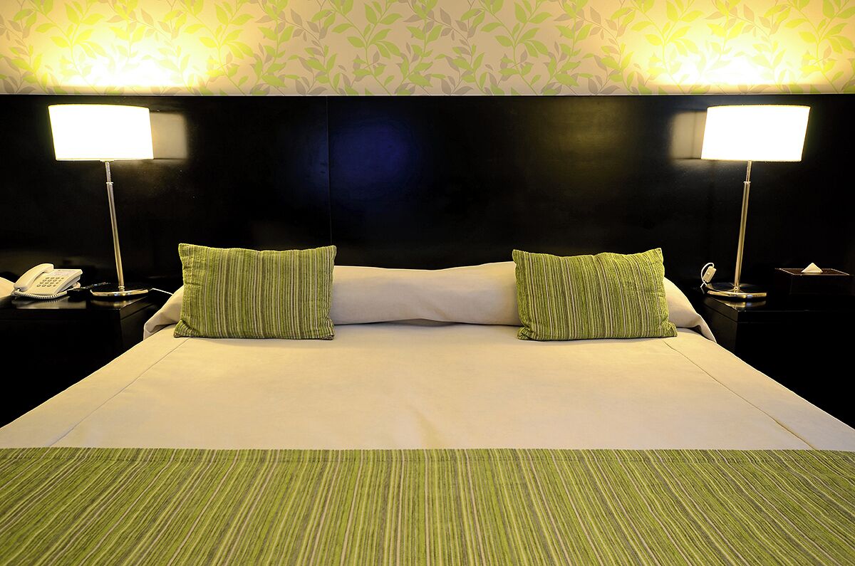 A hotel room with a large bed, two green striped pillows, two bedside lamps, a telephone on the left side, and a tissue box on the right side.
