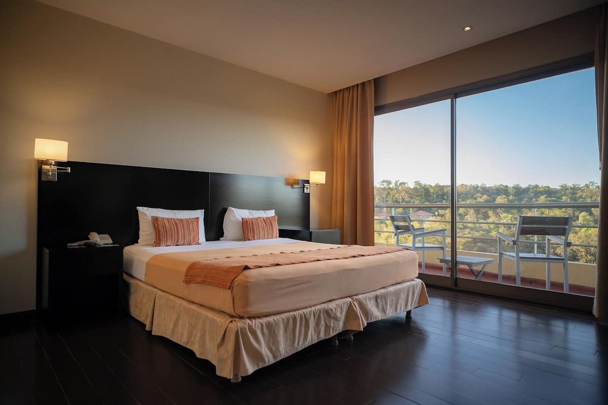 Une chambre d’hôtel avec un grand lit, deux tables de chevet, une petite table et un balcon donnant sur l’extérieur.