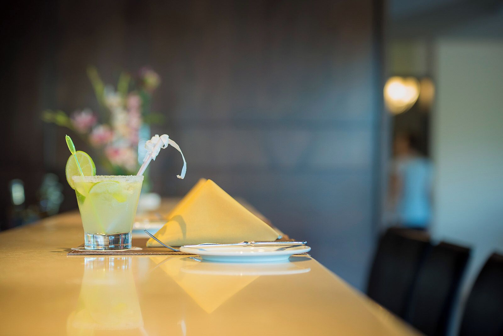 Een cocktail met een limoenpartje en rietje, geplaatst op een tafel met een servetje en een opgevouwen servettenhouder.