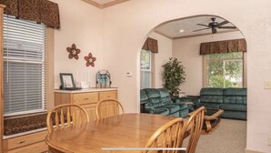 A dining area with a wooden table and chairs, a kitchen area with a stove and cabinets, and a living room with a green sofa and a ceiling fan. - Spacious R&R University Retreat  (Pocatello)