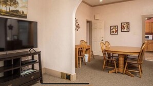 A living room with a flat-screen TV on a black stand, a dining area with a wooden table and chairs, and a kitchen visible through an open doorway. - Spacious R&R University Retreat  (Pocatello)