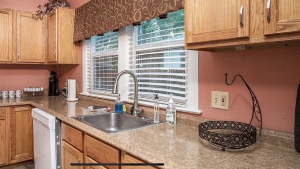 A kitchen with wooden cabinets, a microwave, a sink, and a window with blinds. - Spacious R&R University Retreat  (Pocatello)