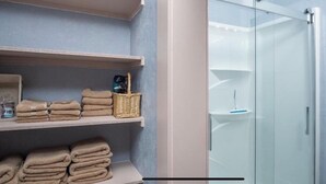 A bathroom with a glass shower enclosure, shelves with towels, and a wicker basket. - Spacious R&R University Retreat  (Pocatello)