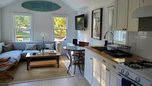 A modern kitchen with white cabinets, a gas stove, and a dining area with a table and chairs. - One Bedroom Hamptons Waterfront Cottage (Hampton Bays)