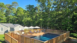A rectangular swimming pool with a wooden deck, surrounded by trees. - One Bedroom Hamptons Waterfront Cottage (Hampton Bays)