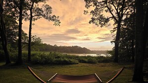 A hammock in a grassy area with trees and a lake in the background. - One Bedroom Hamptons Waterfront Cottage (Hampton Bays)