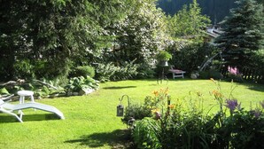 A lush garden with a variety of plants and flowers, a white bench, and a small table. - Small apartment 2-4 pers, wooden log cabin, cozy, quiet, sunny, close to the center (Kleinarl)