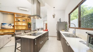 Une cuisine moderne dotée d’un îlot central, d’appareils électroménagers intégrés et d’une grande fenêtre offrant une vue sur l’extérieur.