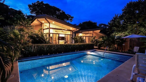 Un hôtel moderne doté d’une piscine, entouré d’une végétation luxuriante et offrant un intérieur bien éclairé.