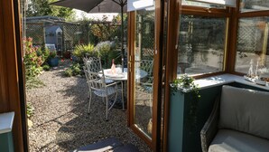 Une véranda avec une table et des chaises, un parasol et une maquette de bateau posée sur une étagère.