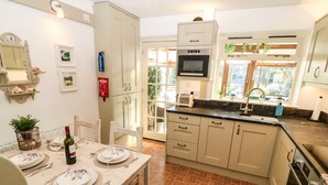 Une cuisine avec un coin repas, comprenant une table dressée pour deux personnes, un four encastré et une fenêtre donnant sur un paysage verdoyant.