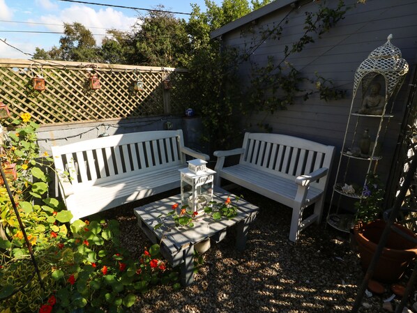 A garden patio with two white benches, a small table, and a decorative birdcage.