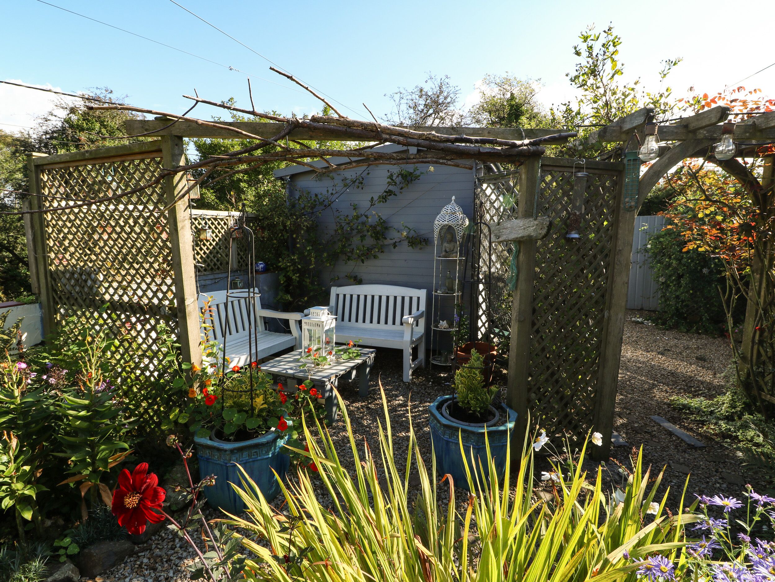 A garden with a wooden pergola, white benches, and potted plants.