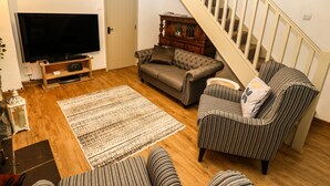 Un salon comprenant un canapé, un fauteuil, un téléviseur, un plancher en bois et un escalier.