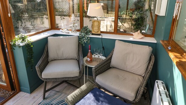 Un coin accueillant avec deux fauteuils en osier, une petite table avec une lampe et une vue sur la verdure grâce à de grandes fenêtres.