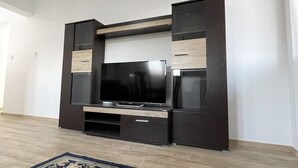 A modern living room with a large flat-screen TV, dark wooden entertainment unit, and a patterned rug.