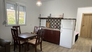 A compact kitchen with a dining area, a refrigerator, and a window with blinds.