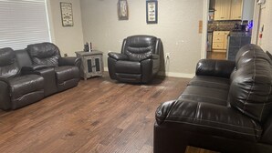 A living room with leather sofas, a small side table, and a wall-mounted light fixture. - Waterfront 2 bedroom home- South Toledo Bend (Florien)