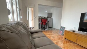Una sala de estar con un sofá de cuero, un mueble bajo de madera para el televisor y una cocina al fondo.