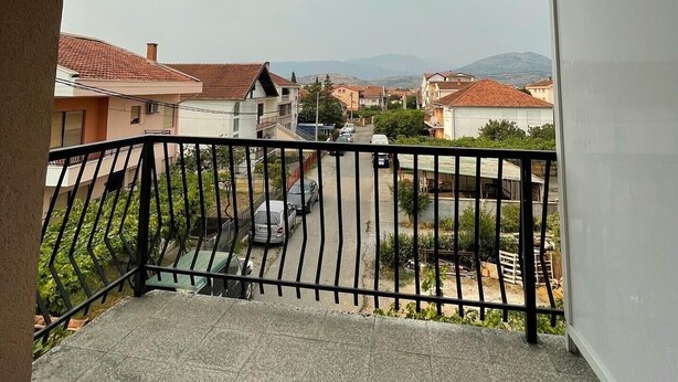 Un balcón con vistas a una calle residencial y montañas al fondo.