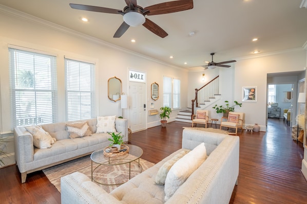A spacious living room with a high ceiling, wooden flooring, and a staircase leading to an upper level.