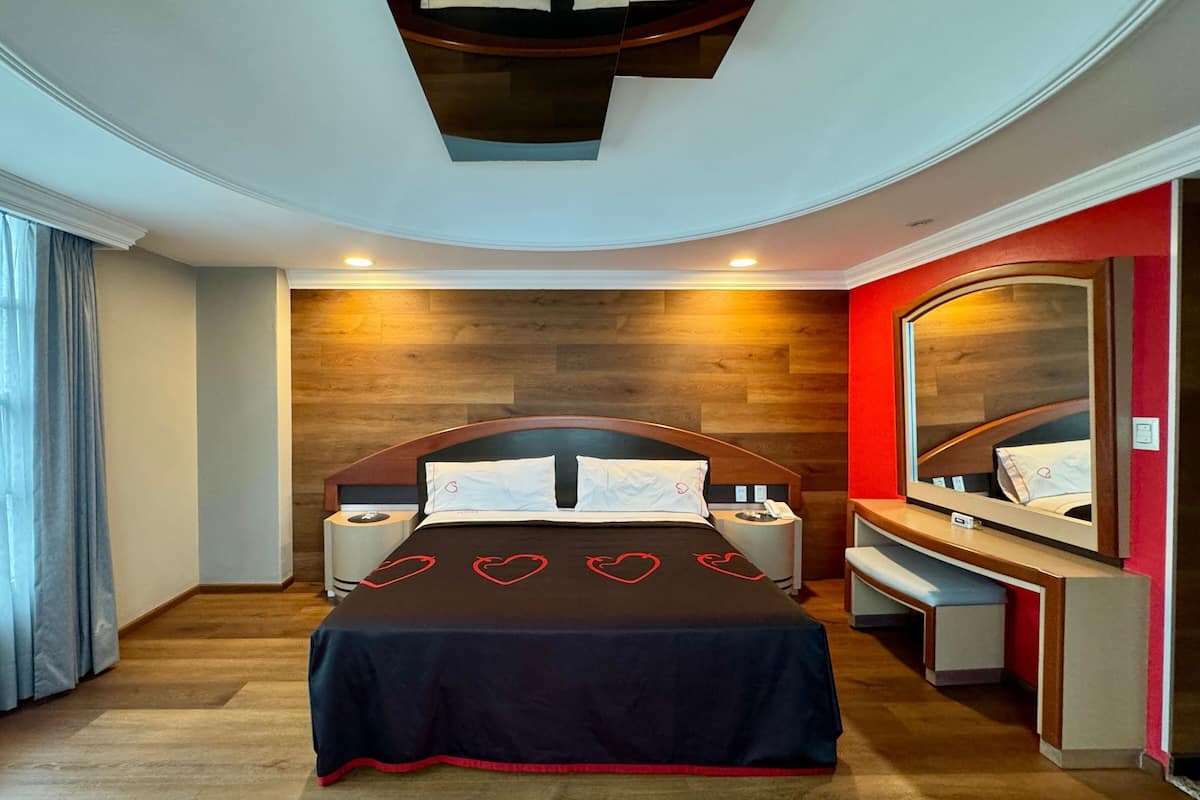 A modern bedroom with a wooden headboard, a large mirror, and a bedside table with a lamp.