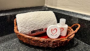 Uma cesta de vime com uma toalha branca, um frasco de sabonete e um porta-sabonete com design de coração.
