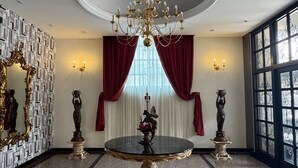 Um quarto luxuoso com uma grande mesa redonda, lustres decorativos nas paredes e um imponente candelabro.