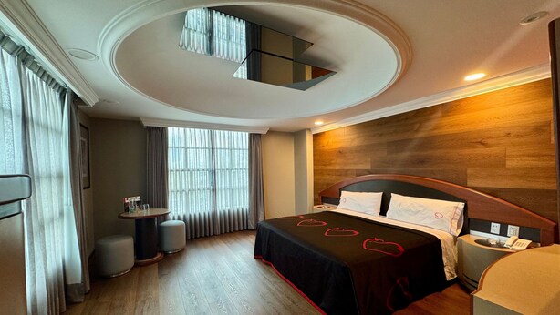 Quarto de hotel moderno com uma cama grande, uma mesinha, uma cadeira e um espelho sobre a cama.