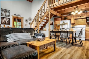 A cozy living room with a leather sofa, wooden coffee table, and a staircase leading to a kitchen area. - Experience serenity near entertainment, stay at our 3-bedroom cabin, Pkwy close! (Pigeon Forge)