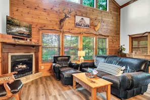 A cozy cabin interior with a fireplace, leather furniture, wooden walls, and deer antlers decor. - Experience serenity near entertainment, stay at our 3-bedroom cabin, Pkwy close! (Pigeon Forge)