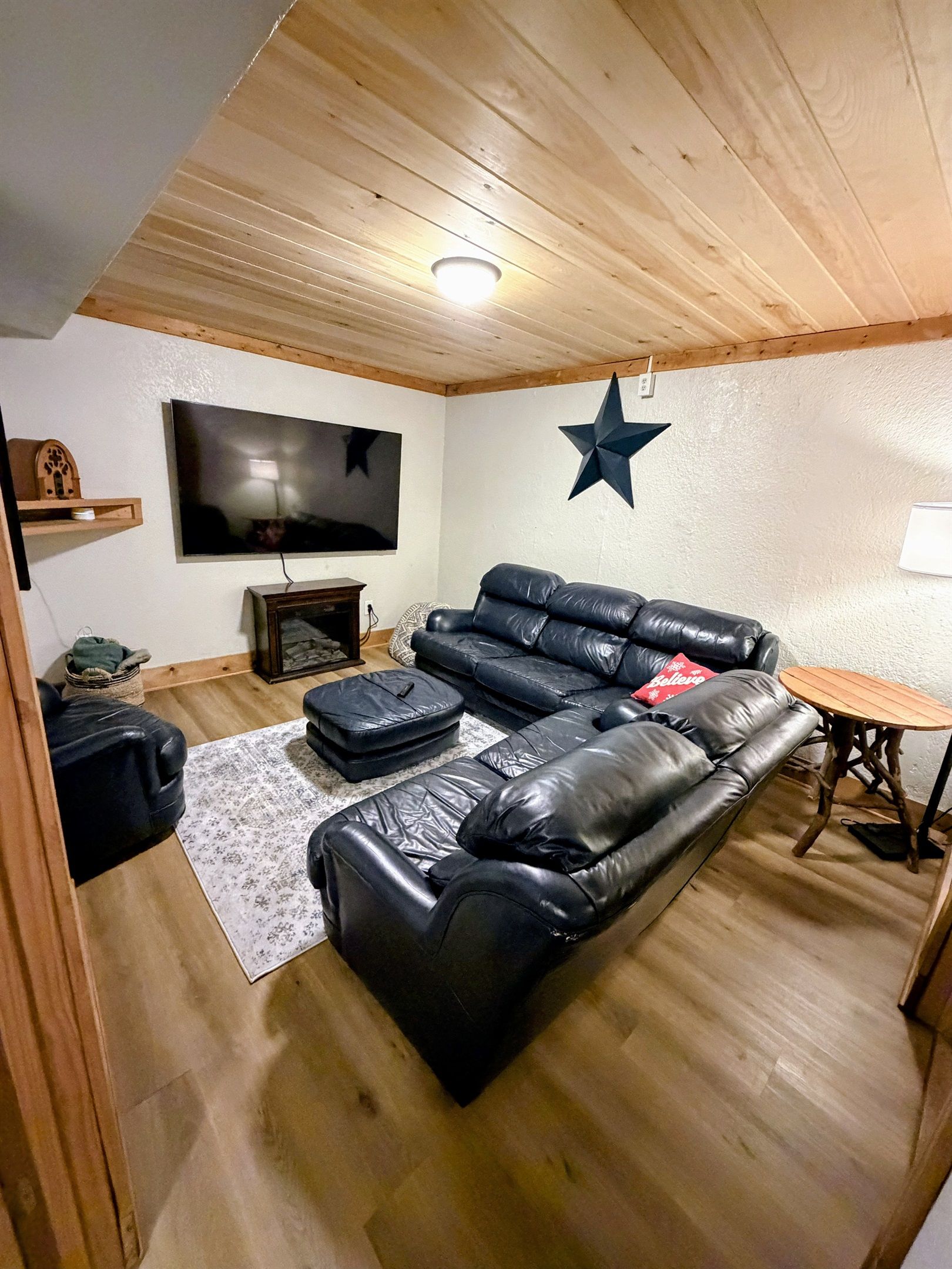 Un salón con un sofá de cuero negro, un televisor de pantalla plana, una decoración con estrellas en la pared y una pequeña mesa de madera.