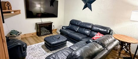 Un salón con un sofá de cuero negro, un televisor de pantalla plana, una decoración con estrellas en la pared y una pequeña mesa de madera.