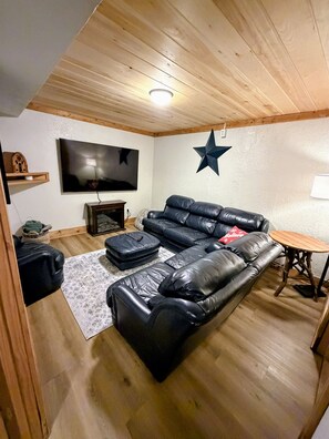 A living room with a black leather sofa, a flat-screen TV, a star decoration on the wall, and a small wooden table.