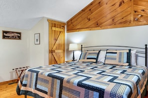 A bedroom with a wooden ceiling, a quilted bedspread, a wooden door, and a framed sign on the wall.