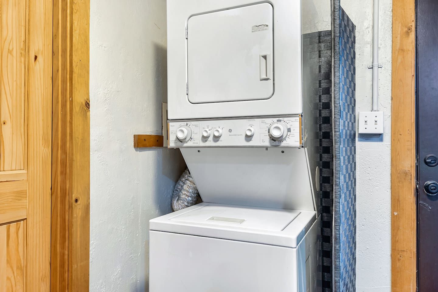 A laundry room with a white washing machine and dryer, wooden door, and tiled wall.