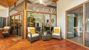 A spacious living area with wicker furniture, a ceiling fan, and large glass doors leading to a garden. - Total Stellar Entire Property 3 Villas Luxurious Oasis Getaway (Playa Langosta, Tamarindo)