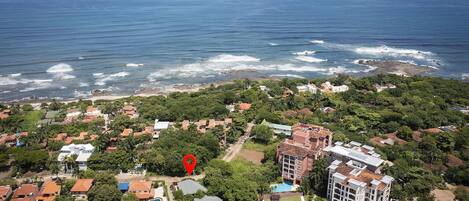 Vista aérea de una zona residencial costera con casas, un lugar marcado y un edificio grande con piscina.