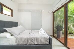 A modern bedroom with a large bed, grey bedding, and a view of greenery through a sliding glass door. - Total Stellar Entire Property 3 Villas Luxurious Oasis Getaway (Playa Langosta, Tamarindo)