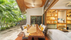 A modern dining area with a long wooden table, wicker sofas, and a view of lush greenery. - Total Stellar Entire Property 3 Villas Luxurious Oasis Getaway (Playa Langosta, Tamarindo)