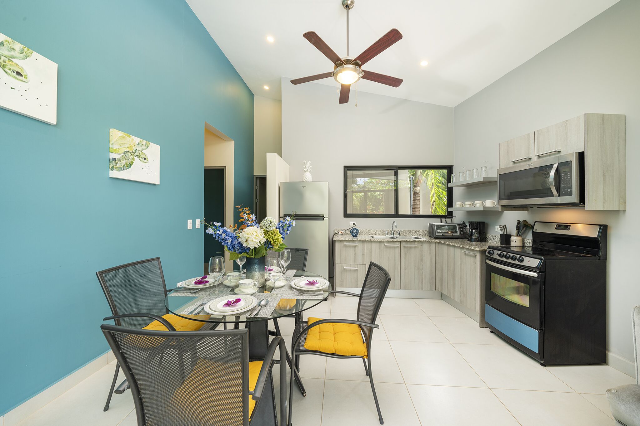 A modern kitchen with a dining area, featuring a ceiling fan, a refrigerator, a microwave, and a stove.