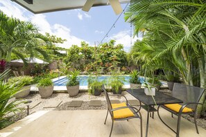 A poolside area with a table and chairs, surrounded by potted plants and a clear blue sky. - Total Stellar Entire Property 3 Villas Luxurious Oasis Getaway (Playa Langosta, Tamarindo)