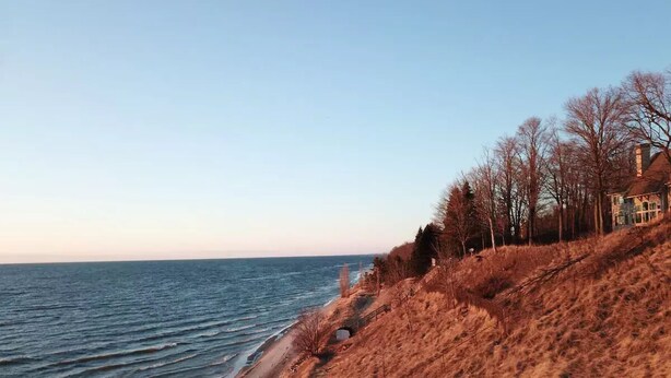 Eine Küstenlandschaft mit Strand, einer grasbewachsenen Böschung und einem Gebäude mit schrägem Dach.