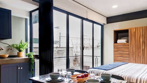 Ein modernes Hotelzimmer mit Essbereich, einem großen Fenster mit Ausblick und einem Bett mit gestreifter Bettdecke.
