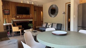 Una cuina moderna amb zona de menjador, panells de fusta, televisió de pantalla plana i nevera.