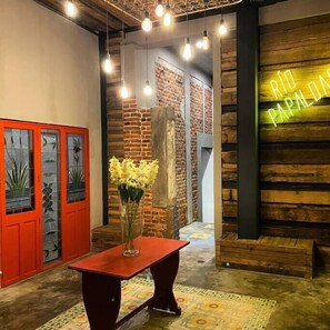 A room with a wooden wall, a neon sign, a vase with flowers, and a red table.
