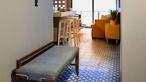Un corridoio con pavimento decorato, una panca in legno, un'area pranzo con sedie e un divano giallo.