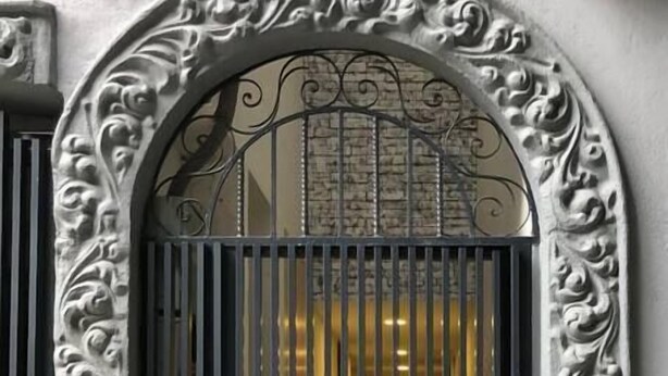 Un cancello in metallo decorato con motivi intricati, incorniciato da un arco ornamentale.