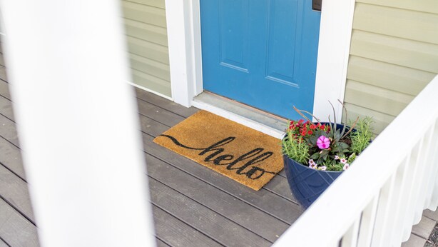 Eine blaue Tür mit einer braunen Fußmatte, auf der 'hello' steht, und ein Blumentopf mit Blumen.